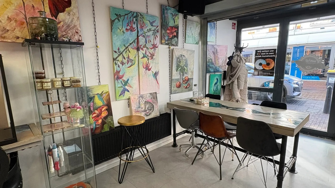 De voorkant van de salon met schilderijen aan de muur en een tafel bij het raam